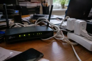 A standard ISP router and smart plugs on a cluttered desk representing home network congestion